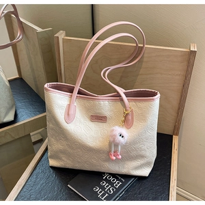 Detail of cream tote bag with pink trim, featuring embossed patterns and pom-pom charm