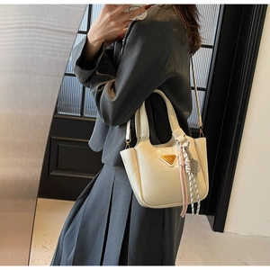 Détail du sac seau en cuir blanc crème avec logo triangle doré et pendentif tressé
