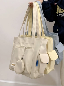 Detail view of large tote bags in cream, yellow, and blue with front pockets and small pouches