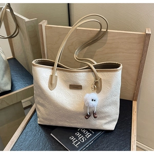 Detailed macro of cream tote bag with embossed lotus patterns and fluffy charm