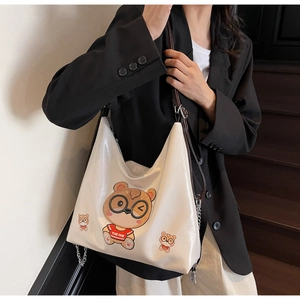 Detail of cream tote bag with bear print and wide shoulder strap on model in suit