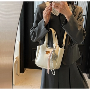 Détail d'un sac cabas en cuir crème avec logo métallique et pendentif en corde tressée