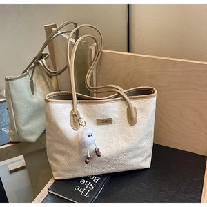 Detail of cream embossed leather tote bag with brown straps and plush ball charm decoration