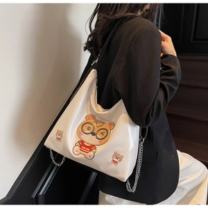 Detail of white glossy tote featuring a cartoon bear print and decorative silver chains