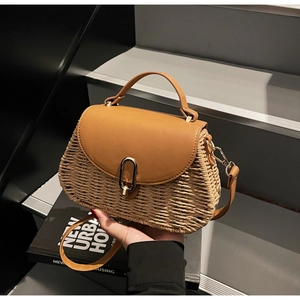 Detail of woven straw bag showing brown leather flap and golden oval metal lock