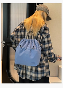 Detail of light blue nylon drawstring backpack with front pockets on model back