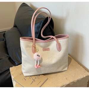 Detail of embossed tote bag with pink trim, unique patterns, and a plush doll pendant
