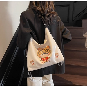 Detail of white glossy leather hobo bag featuring a cartoon bear print and chain accents