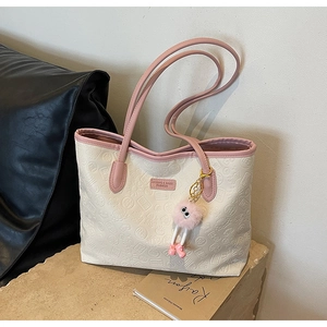 Detail of cream embossed leather tote bag with pink trim and fuzzy eye charm on stone