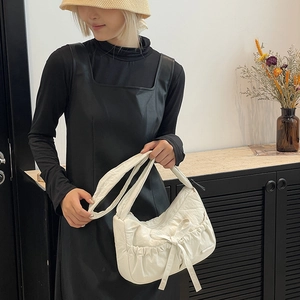 Detail of a creamy white nylon tote bag featuring a decorative bow and pleated texture