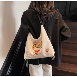 Close-up of white leather tote bag featuring cartoon bear prints and metal chain detail