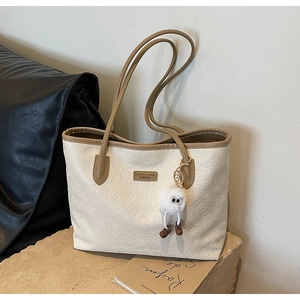 Close-up of embossed cream tote bag with floral patterns and plush charm on stone surface
