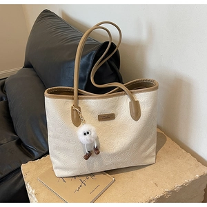 Detail of off-white embossed leather tote bag with dark brown handles and plush charm