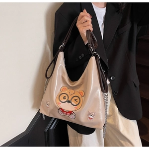 Detail of glossy beige tote bag featuring a cute cartoon bear and silver chain straps