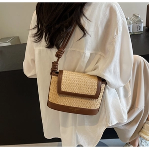 Detail of a woven straw shoulder bag with brown leather trim and knotted strap on a model