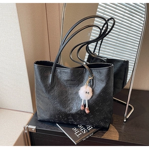 Detail of black tote bag featuring embossed traditional characters and plush charm