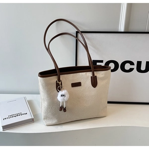 Detail of cream tote bag with embossed floral texture and plush charm on wave stand