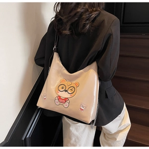 Detail view of large beige glossy tote bag featuring a cute cartoon bear print and chain
