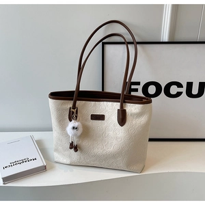 Detailed view of beige tote bag with embossed patterns and plush monster charm
