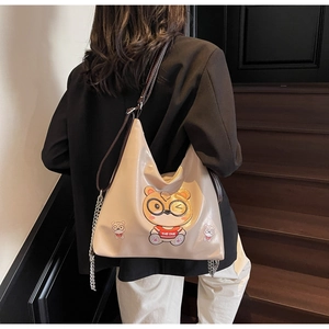 Close-up of cream tote bag with cartoon bear print and chain strap detail on model