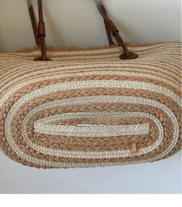 Close-up of woven straw tote with striped texture, raw fringe edges and leather handles