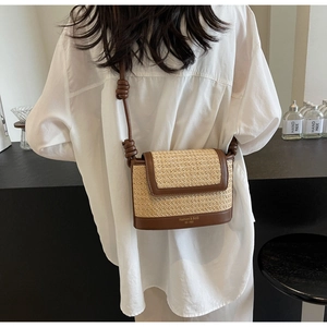 Detail of a straw crossbody bag featuring a knotted brown leather strap and brand engraving