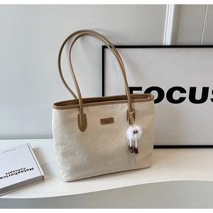 Detail of cream tote bag with embossed lotus patterns and white plush charm on a desk