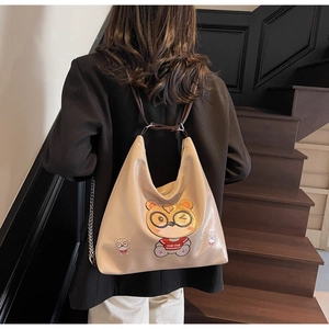 Model wearing a beige PU leather half-moon tote bag with cartoon bear on dark stairs