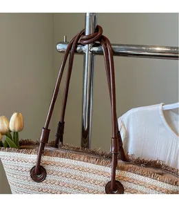 Detail of woven straw tote bag featuring frayed edges and brown leather shoulder straps