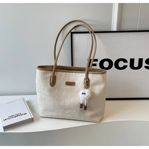 Close-up of beige embossed leather tote bag with floral patterns and a plush charm