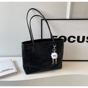 Close-up of black embossed tote bag featuring a cute white plush monster charm accessory