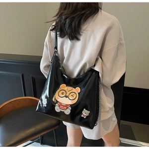 Detail of black glossy tote bag featuring a cute cartoon bear patch and metal chain strap