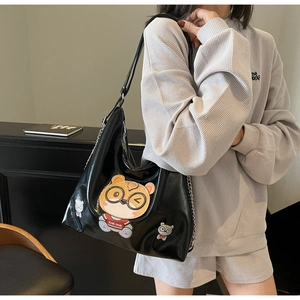 Detail of glossy black tote bag with cartoon bear patches and metal chain on a model