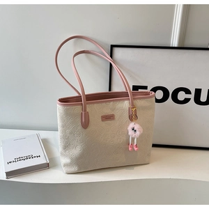 Detail of a beige tote bag featuring pink handles and an embossed relief pattern surface
