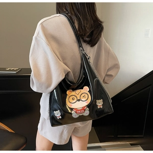 Detail of a large black glossy tote bag with cartoon bear patches and chain strap