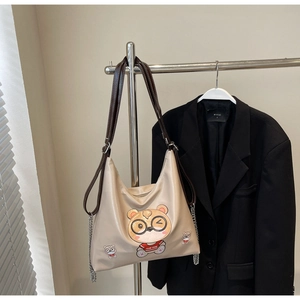 Detail of beige tote bag with cartoon bear print, leather straps and silver chain decoration
