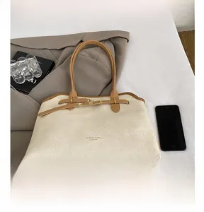 Detail of cream tote bag with brown handles and gold lettering next to a phone for scale