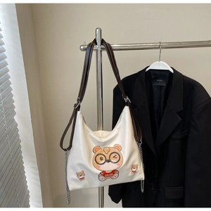 Detail of white tote bag with cartoon bear print, brown strap, and silver chain decoration