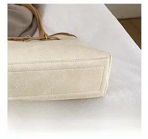 Detail showing precise stitching on cream tote bag with contrast brown handle and gold hardware