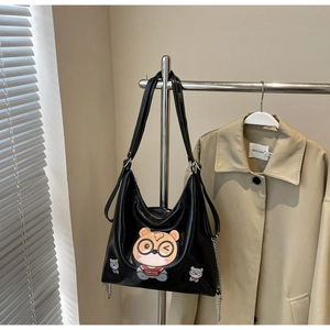 Detail of black glossy tote bag with cartoon bear patch and stylish silver chain