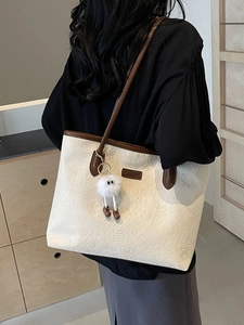 Minimalist cream tote bag with textured patterns and plush charm on female shoulder
