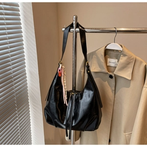 Détail d'un sac cabas noir brillant avec base plissée et breloque en cordon coloré
