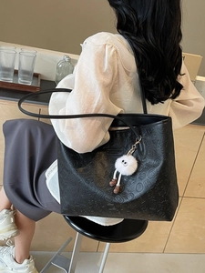 Black embossed leather tote bag with unique cultural patterns and a plush charm