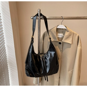 Détail du sac hobo noir brillant avec large bandoulière et fermeture éclair dorée