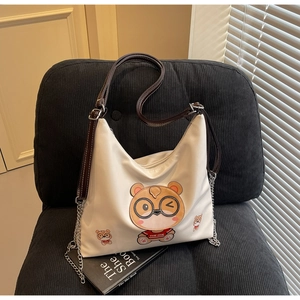 Detail of white tote bag with cartoon puppy embroidery and metal chain on a sofa