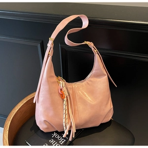 Détail d'un sac hobo rose avec des pompons en cuir et des garnitures métalliques dorées