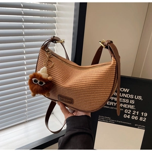 Detail of woven crescent bag featuring leather strap, gold hardware, and plush charm