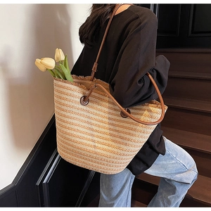 Detail of woven straw tote bag featuring brown leather straps and stylish fringe trim