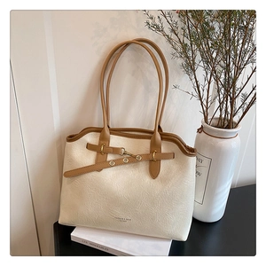 Detail of minimalist leather tote bag featuring gold buckle closure and cross strap design