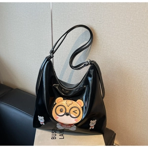 Detail of glossy black tote bag featuring a large cartoon bear patch and shiny texture